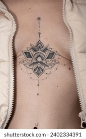 intricate, symmetrical lotus-like tattoo adorns the upper chest, framed by an open textured jacket
