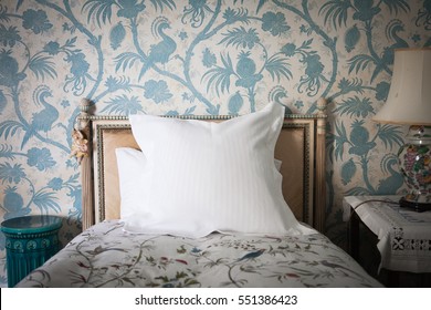 Intricate wooden headboard single bed against blue and white antique bird wall paper