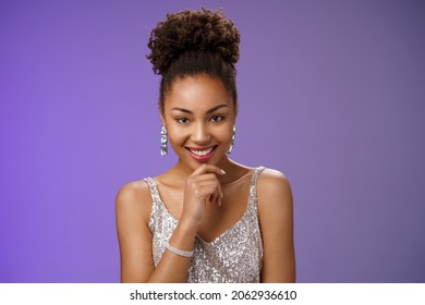 Intrigued creative young african-american devious 20s girl afro hairstyle in silver luxurious dress partying touching chin smirking mysterious have excellent idea inspired planning, blue background