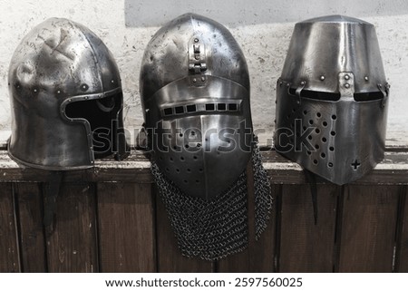 An intriguing display featuring three medieval helmets, crafted from metal and displayed on a wooden background. A representation of historical artistry, tradition, and protection in medieval times