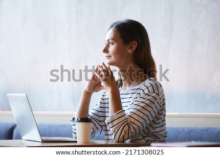 Introspective purposeful young lady sitting at table in modern cafe and thinking of new internet project