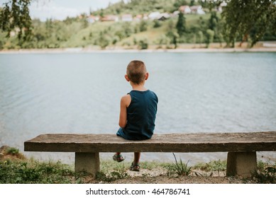 Introverted boy sitting on the bench by the lake - Powered by Shutterstock