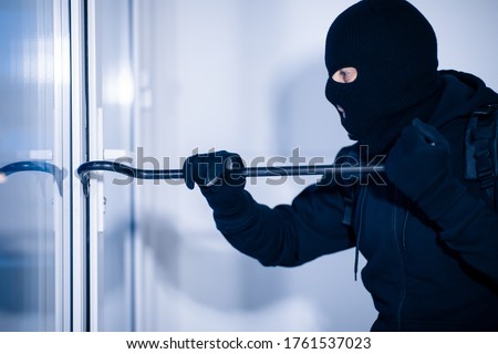 Intrusion Concept. Side view portrait of disguised prowler breaking house or office door with crowbar