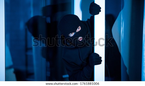 Intrusion\
Concept. Villain with black hat sneaking into apartment, lurking\
out open glass door, banner, copy\
space
