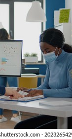 Invalid businessman and african employee with protective mask against coronavirus working together at financial project in new normal start up company, compering statistics looking at computer