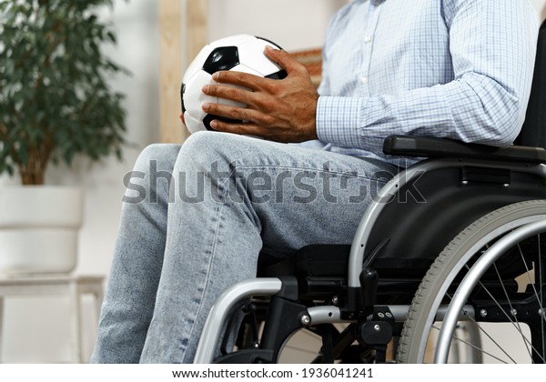 Invalid or disabled man sitting on wheelchair and\
holding soccer ball