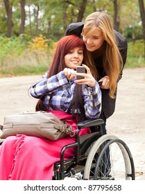 invalid girl on the wheelchair with mobie phone and friend outdoors