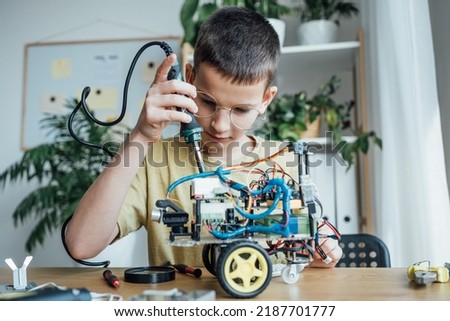 Inventive teen kid constructing robot in the studio. Concentrated boy creating robot at lab. Early development, diy, innovation, modern technology concept. Stem education