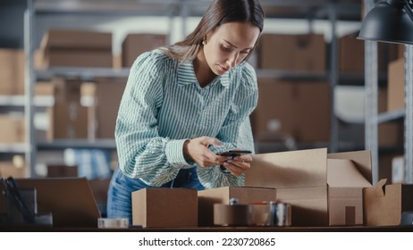 Inventory Manager Using Smartphone to Scan a Barcode on Parcel, Preparing a Small Cardboard Box for Postage. Young Female Small Business Owner Working on Laptop in Warehouse with Colleague. - Powered by Shutterstock