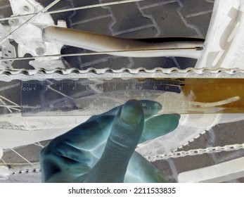 Inverted colors - Close view on manual checking of bike chain wear and tear degree by measuring the length of segments with a transparent plastic ruler.