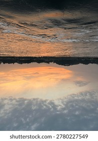 Inverted perspective of a dramatic sunset over a river with dark water and orange sky