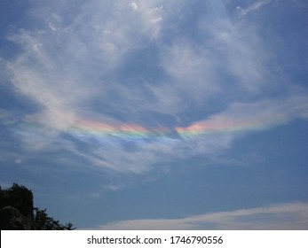 An inverted rainbow with very saturated colors, suspended among fluffy clouds under deep blue sky