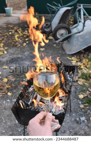 inverted reflection of the flame from the barbecue in a glass of white wine against the background of garden wheelbarrows piled in a heap