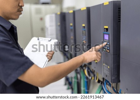 Inverter Control Room System Electrical engineers monitor the controller's frequency and current and record the data to the paper in his hand.