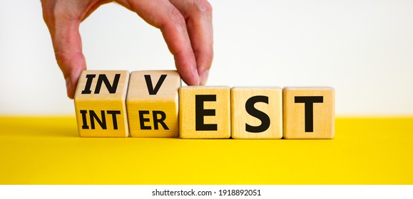 Invest or interest symbol. Businessman turns wooden cubes and changes the word 'invest' to 'interest'. Beautiful yellow table, white background, copy space. Business and invest or interest concept. - Shutterstock ID 1918892051