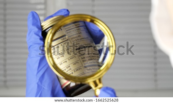 Investigating\
ingredients of medicines, chemicals used in pills capsules inside\
box using magnifying glass, gloved\
hand.