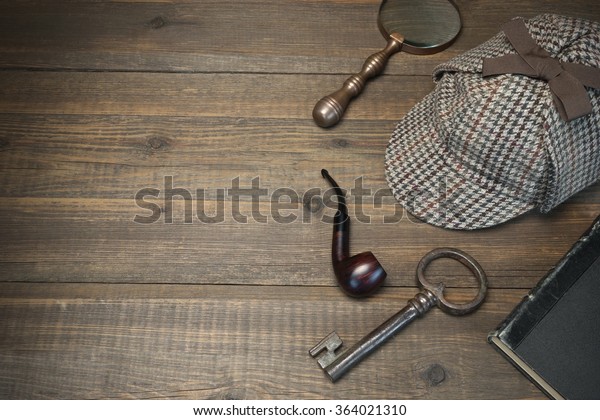 Investigation Concept.
Private Detective Tools On The Wood Table Background. Deerstalker
Cap, Old Key  And Book, Tobacco  Pipe, Vintage Magnifying Glass.
Overhead View