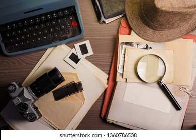 Investigator desk with confidential documents, camera, magnifying glass, vintage typewriter and hat. Secret documents investigation concept.