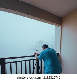 Investigator Or Private Detective Or Reporter Or Paparazzi Setting Tripod For Taking Photo From Balcony Of A Building.