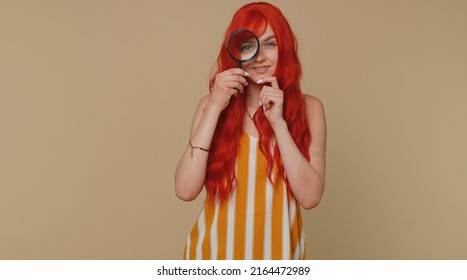 Investigator Researcher Scientist Woman Holding Magnifying Glass Near Face, Looking Into Camera With Big Zoomed Funny Eyes, Searching, Analysing. Young Redhead Girl Isolated Alone On Beige Background