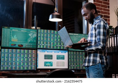 Investment agency stock market trader having laptop analyzing trend moves using real time data. Sales consultant reviewing trading profits using index analytics while standing near modern workstation.