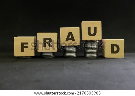 Investment scam, fraud and Ponzi scheme concept. Stack of coins on wooden blocks with word fraudulent in dark black background.