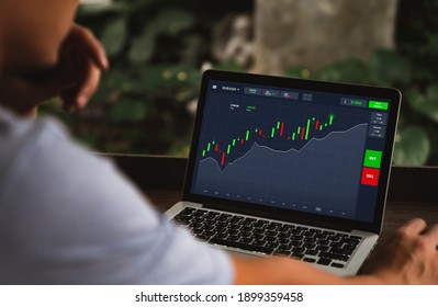 Investment, Shares, Online Trading And Stock Market Concepts. Asian Man Sitting Looking Analyze Stocks Price On Online Marketplace On Laptop Computer Before Buying Investing While Working At Home