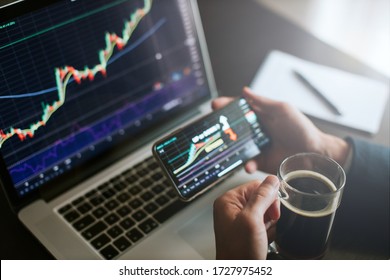 investment stockbroker predicting bitcoin price trend movement using laptop and phone. Crypro trader financial manager analyzing stock graph. Manager using multiple devices and drinks coffee.
