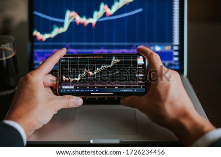 investment stockbroker risk analysis graph on phone screen. Trader using multiple devices for stock price prediction.