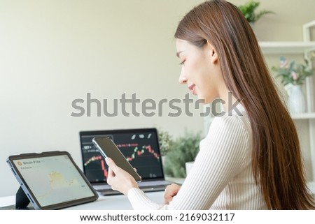Investor analyzing exchange market, asian young business woman trader on graphic charts on laptop computer, hand in using smartphone for trading stock, looking at screen with diagrams at home office.