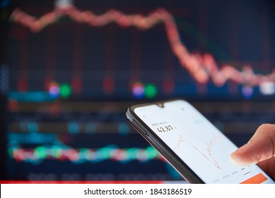 Investor analyzing stock market investments on a smartphone. Person trading stocks on a smartphone. Falling share prices at the stock exchange. Stock market crash. Trader at the stock exchange.