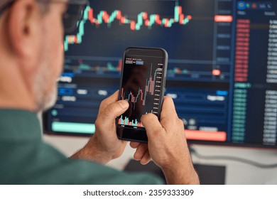Investor trader broker analyzing financial crypto stock trade market on smartphone risk digital price data in mobile app buying bank shares, doing investment strategy analysis on phone. Over shoulder.