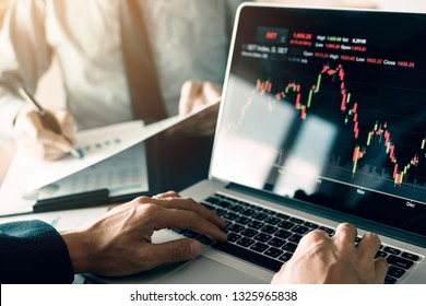 Investors are using laptops entering investment websites stocks market and partners are taking notes and analyzing performance data.