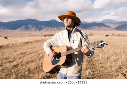 An inveterate cowboy with a cigarette in his mouth walks through a field of dry grass and plays the guitar. Portrait of an American rural guitarist in the mountains. Man is herding cows with a guitar - Powered by Shutterstock