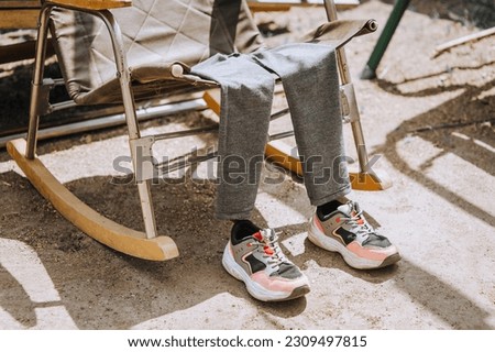 An invisible man, a ghost in children's women's clothing and sneakers, is resting while sitting on a rocking chair outdoors. Photography, idea concept, disappearance.