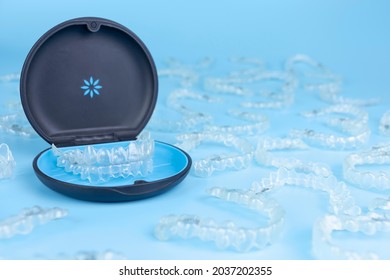 Invisible retainers case with orthodontic aligner brackets thrown around. Black plastic dental container for invisalign braces on blue background