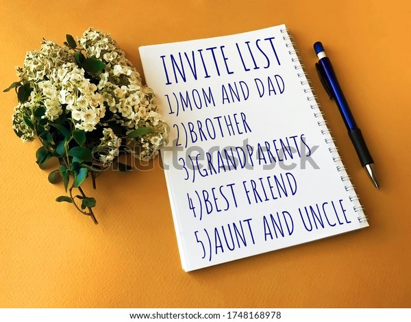 Invite list on a white Notepad for the wedding\
day.Notepad, Pen and flowers on a yellow background.The wedding\
fuss.Photos for the\
wedding.