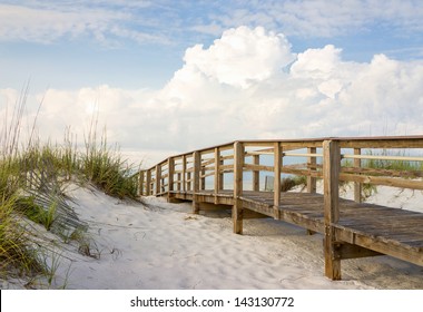 Inviting boardwalk through the sand dunes on a beautiful beach in the early morning. Beautiful puffy clouds in the sky.