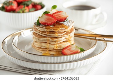Inviting breakfast composition featuring a stack of golden pancakes topped with fresh strawberries and syrup, served on a white plate