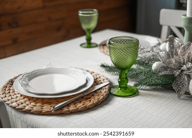 An inviting dining table features green glassware, woven placemats, and white dishware, complemented by elegant center decorations, perfect for a cozy meal or gathering.