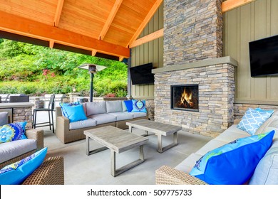 Inviting Interior Of Covered Patio Area  In Tacoma Lawn Tennis Club. Stone Fireplace, Wicker Furniture With Beige Cushions And Bright Blue Pillows. Northwest, USA