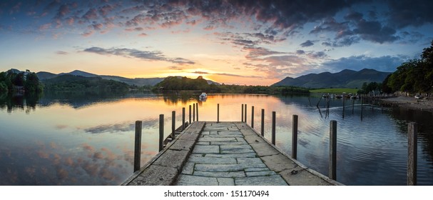 Inviting jetty leading to a dramatic sunset reflected in a perfectly still Derwent Water, Lake District, UK.