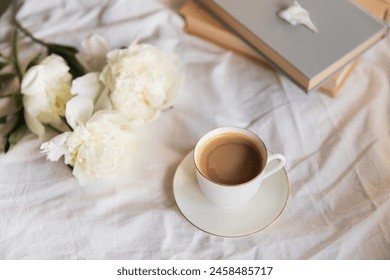 An inviting scene of a warm coffee cup and lush peonies on a bed, capturing the vibe of a relaxed morning. The soft natural light, tranquility atmosphere. Morning in bed aesthetic concept - Powered by Shutterstock