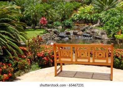 Inviting Wooden Bench In Beautiful Tropical Yard With Soothing Water Feature.