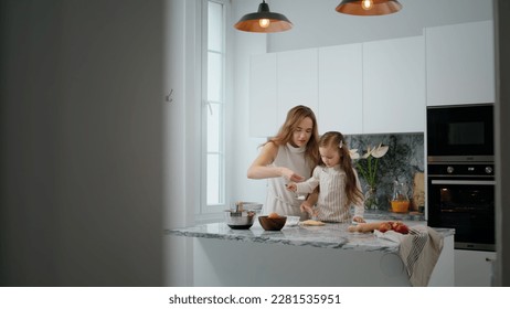 Involved mom and child kneading dough on table. Cute family preparing cookies pastry at contemporary home. Mother daughter cooking at kitchen together. Little girl helping woman in modern interior - Powered by Shutterstock