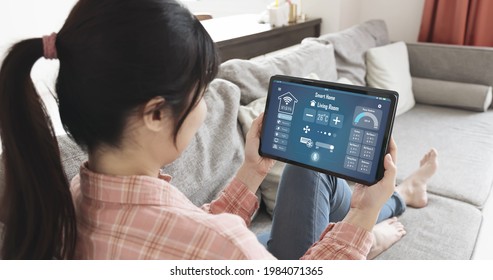 Iot Smart Home Concept - Rear View Of Asian Woman Ask Digital Tablet To Set Temperature Of Air Conditioner More Higher By Voice At Home And All The Electric Meter In House Getting Energy-efficient