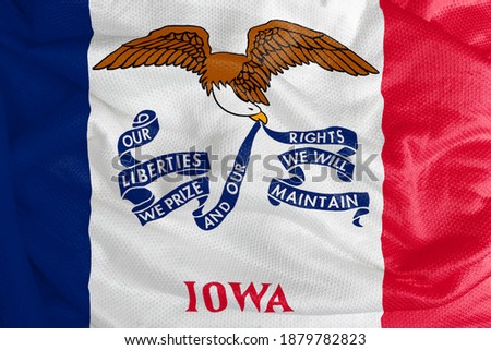 The Iowa flag has three vertical stripes in the colors blue, white, and red, within the white strip the name of the state under an eagle holding a ribbon with the motto of Iowa. 