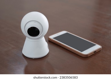 IP Camera. CCTV wireless IP security camera with 360 degrees rotating head with a smartphone on the table, Concept of home security system