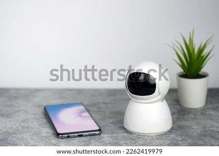 IP Camera.  CCTV wireless IP security camera with 360 degrees rotating head with a smartphone on the table, Concept of home security system for surveillance and protection, controlling via smartphone 