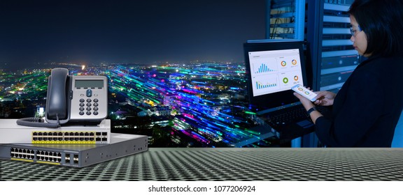 IP Telephone and Network switch 24 port gigabit and System administrator working in data center and blending with smart city at night for high speed telecommunication.
